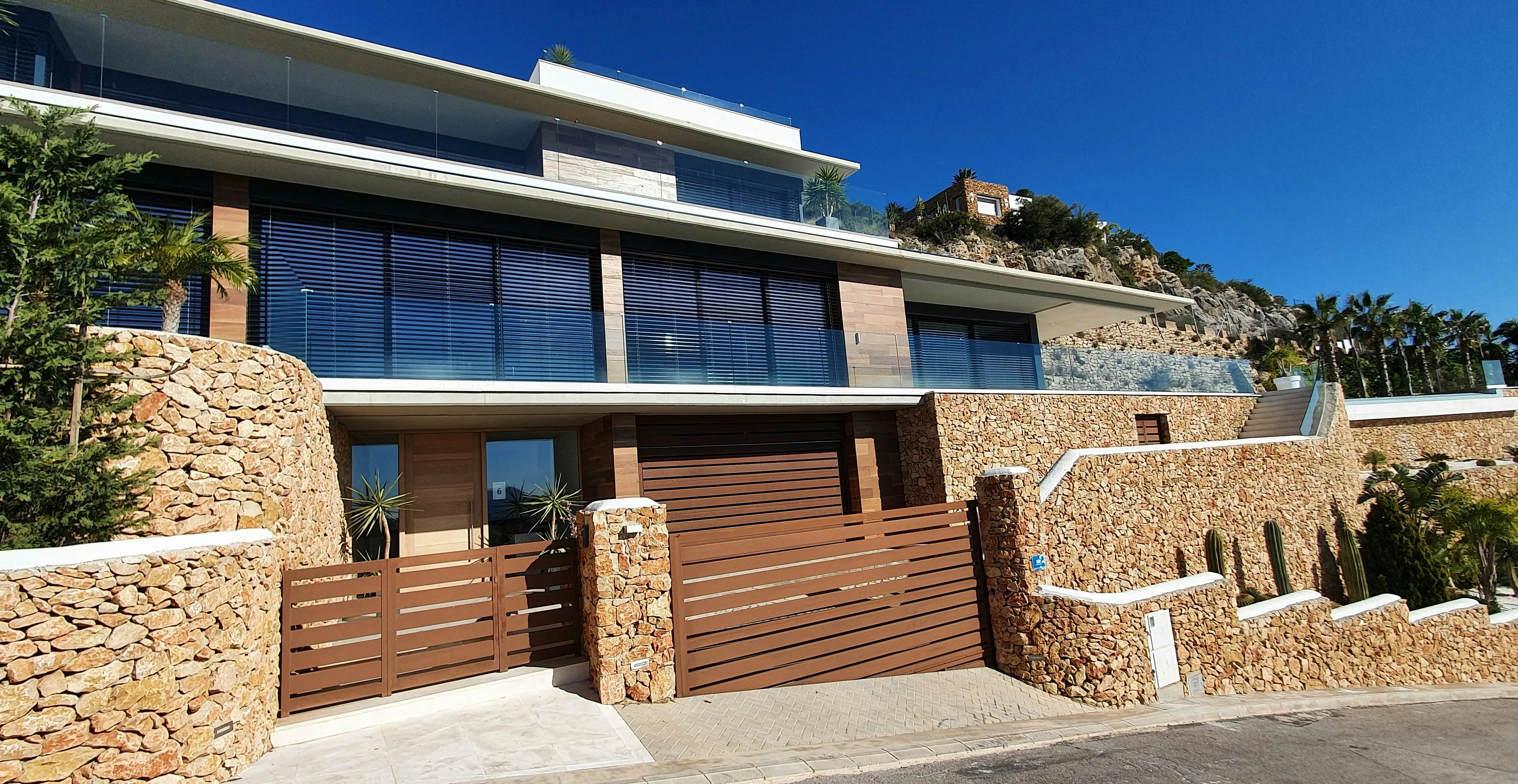 Villa moderne avec façade en pierre, grandes baies vitrées et portail en bois